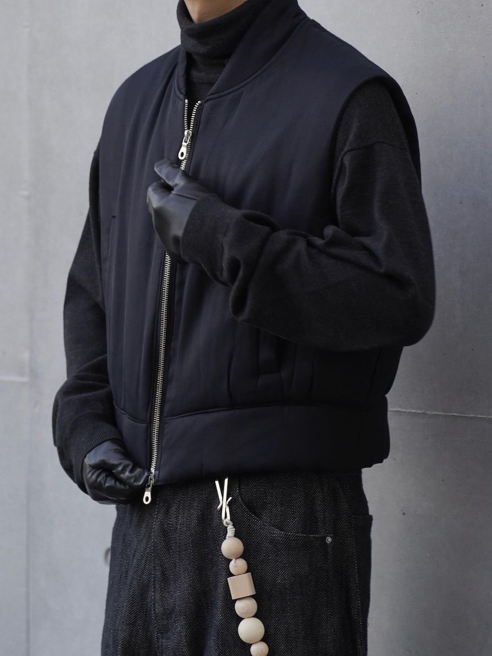 ブラック系のベスト、グレー系のニット/セーター、ブラック系のデニムパンツを着用したメンズの冬コーディネートの2枚目の写真