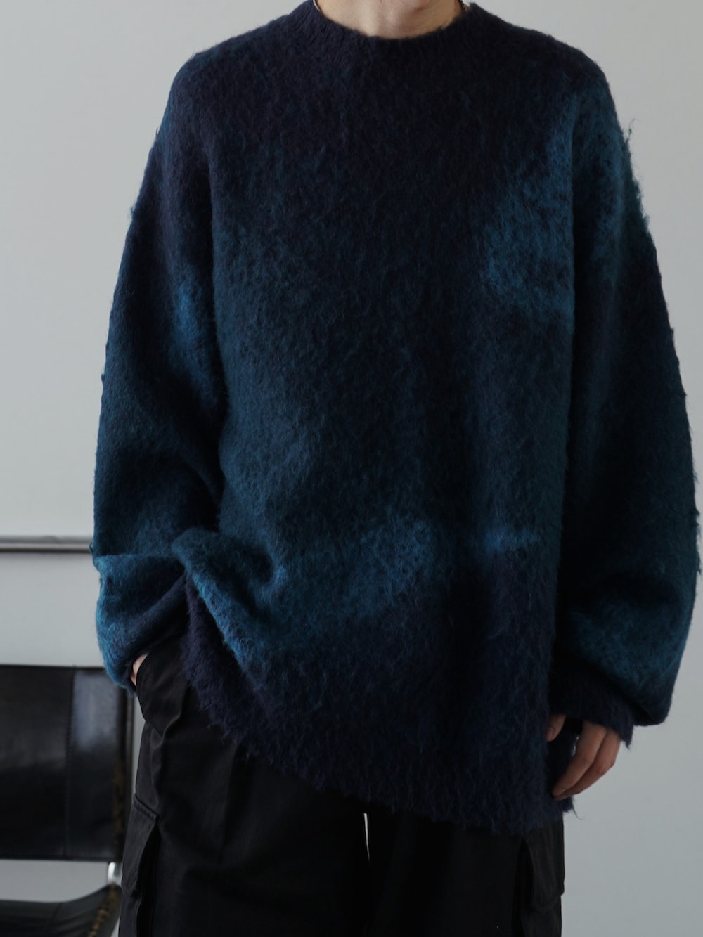 グレー系のチェスターコート、ブルー系のニット/セーター、ブラック系のスラックスを着用したメンズの冬コーディネートの3枚目の写真