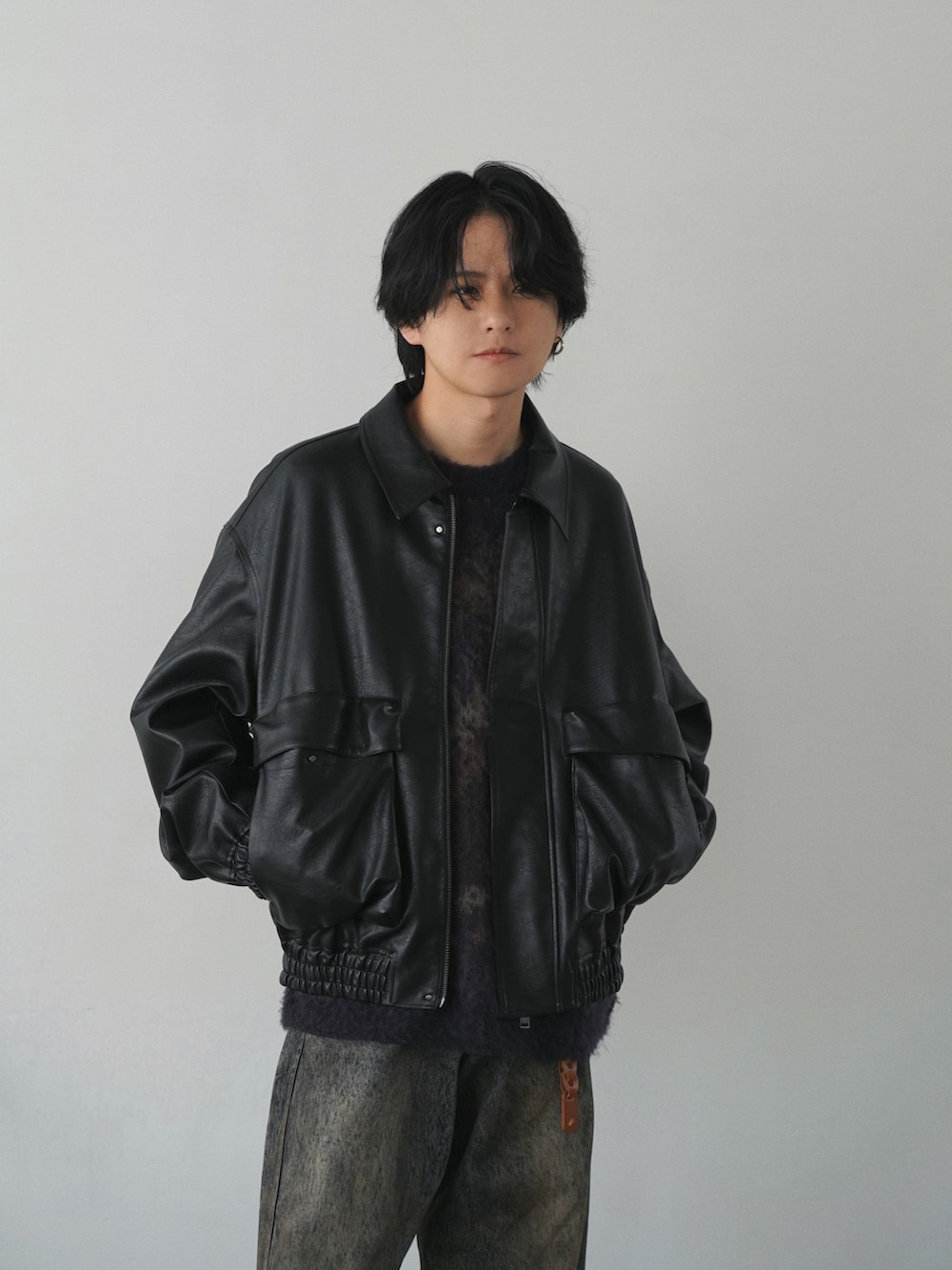 ブラック系のブルゾン、ブルー系のニット/セーター、ブルー系のデニムパンツを着用したメンズの秋コーディネートの2枚目の写真