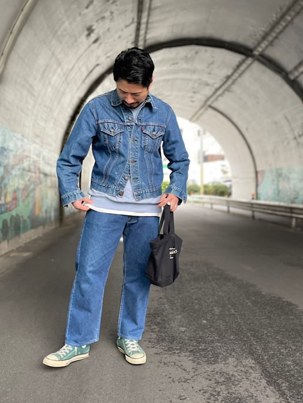 ブラック系のトートバッグ、グリーン系のスニーカー、ブルー系のデニムパンツを着用したメンズの春コーディネートの2枚目の写真