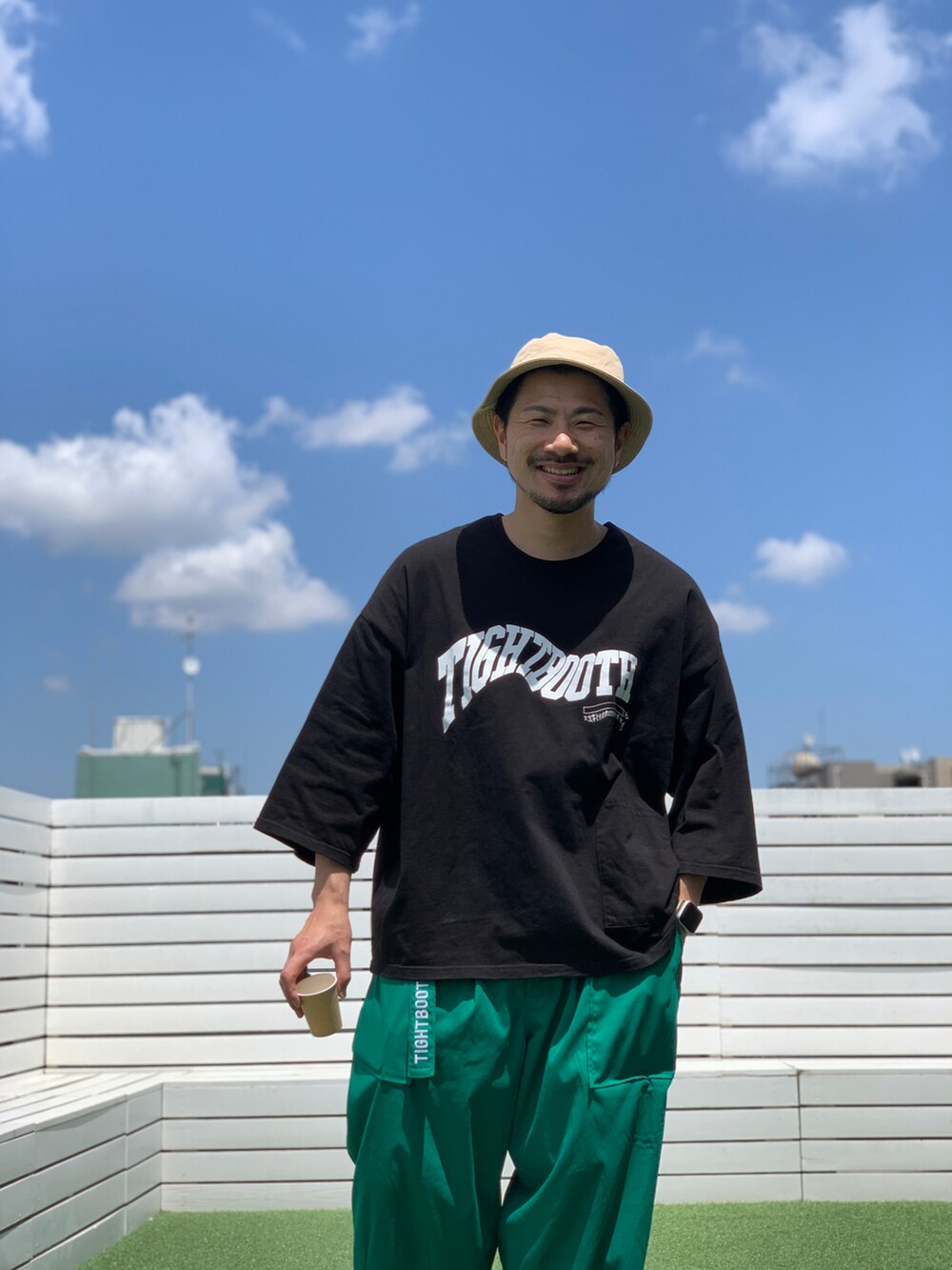 ブラック系のトップス、グリーン系のパンツ、ベージュ系のハットを着用したメンズの夏コーディネートの2枚目の写真