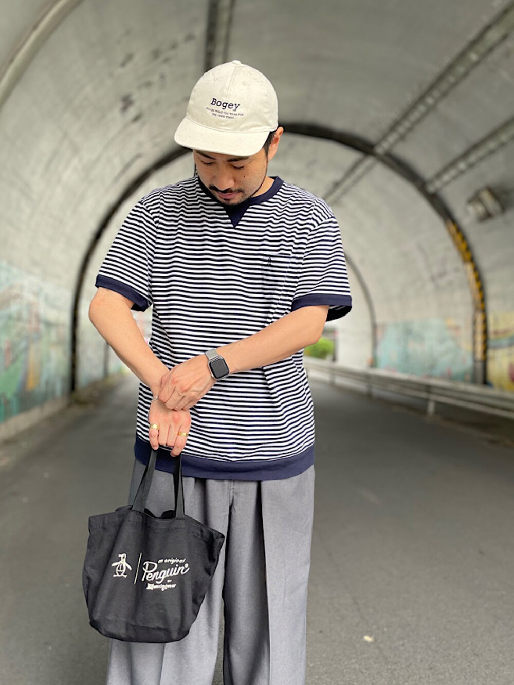 ブラック系のトートバッグ、グレー系のスラックス、ブラウン系のシューズを着用したメンズの夏コーディネートの2枚目の写真