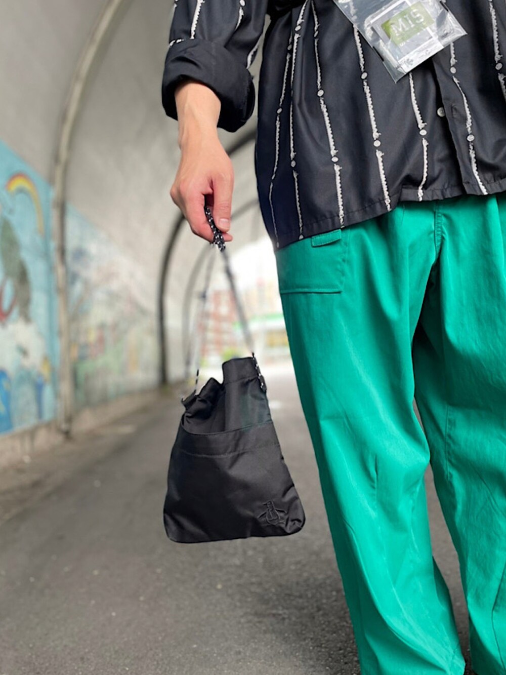 ブラック系のショルダーバッグ、ホワイト系のスリッポン、グリーン系のパンツを着用したメンズの春コーディネートの2枚目の写真