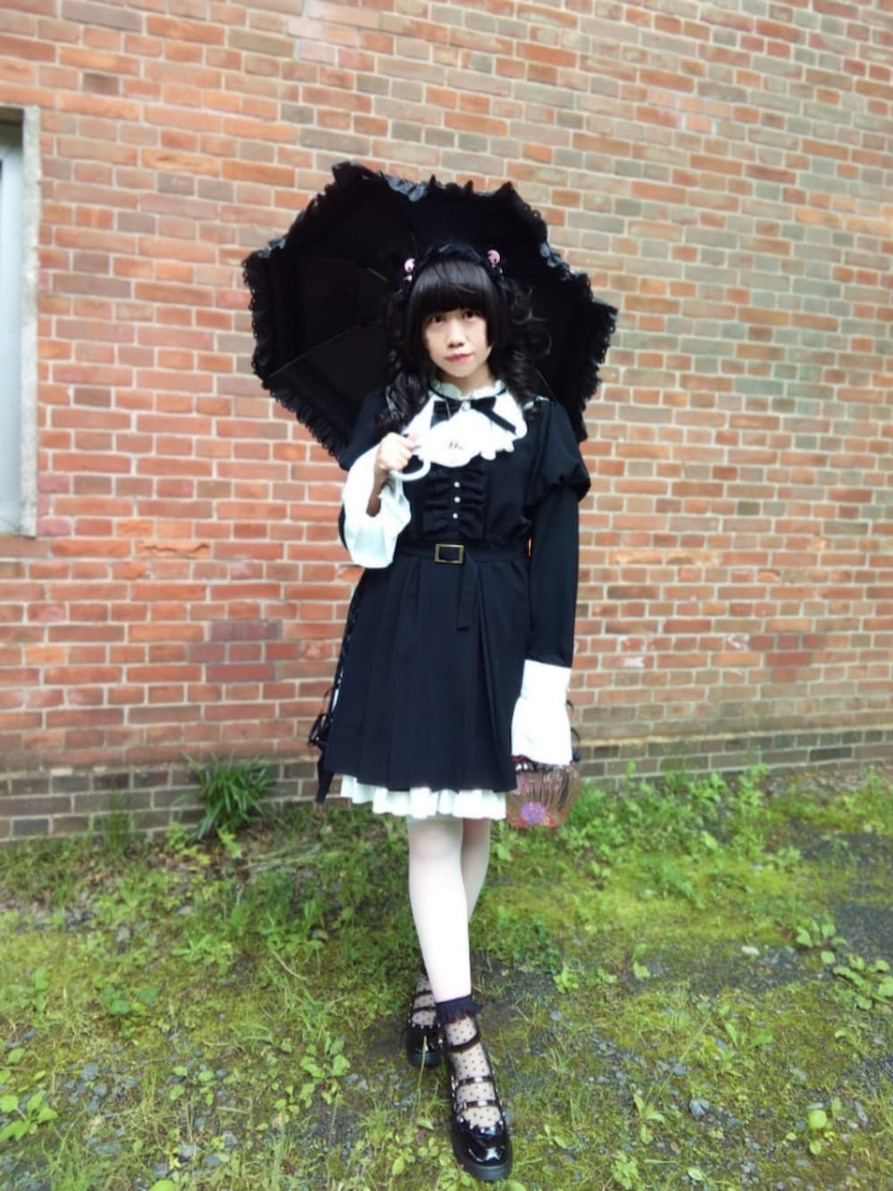 ブラック系のワンピース、ブラック系のパンプス、ピンク系のハンドバッグを着用したレディースの春コーディネートの2枚目の写真