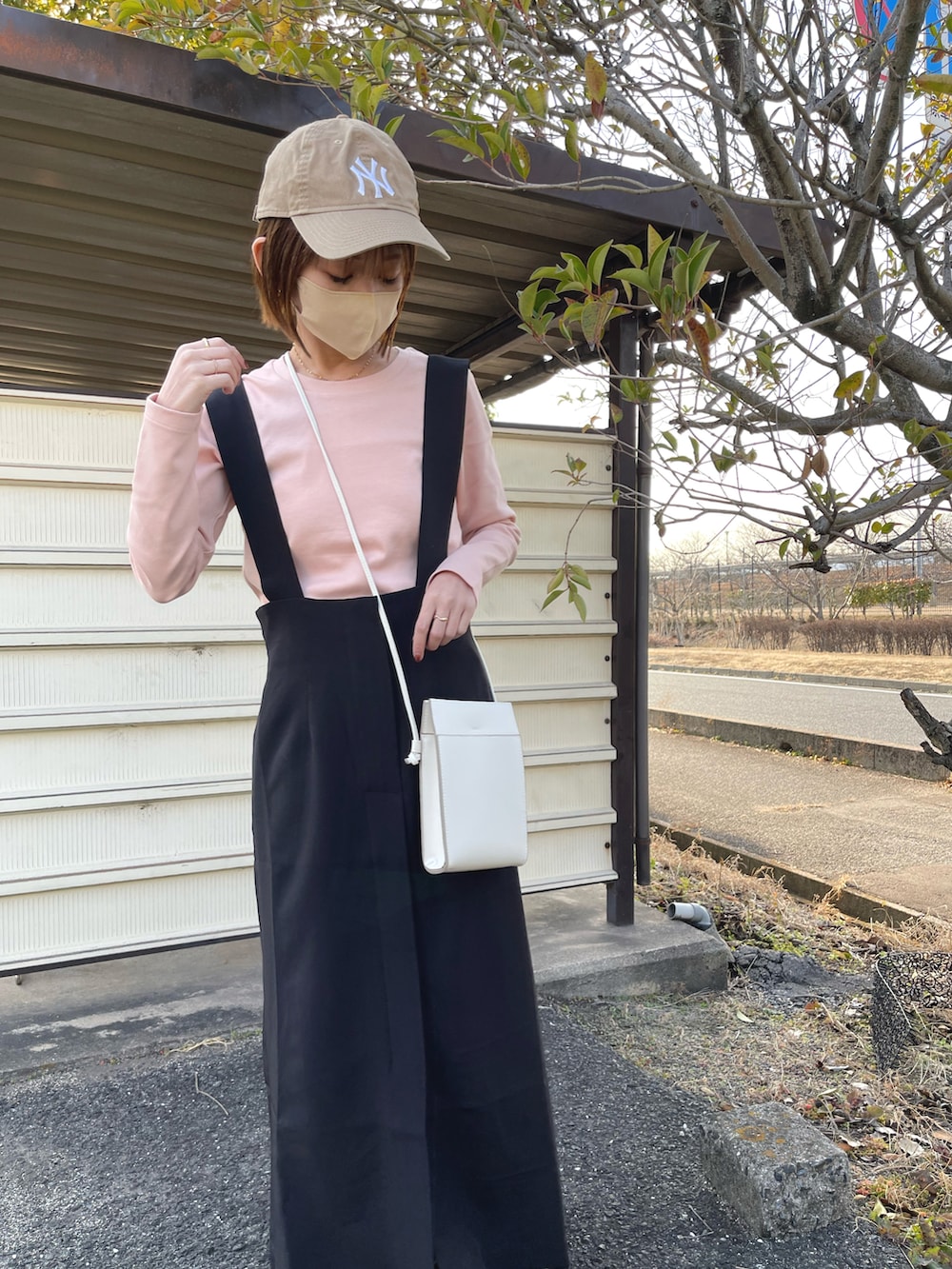 ブラック系のジャンパースカート、ピンク系のTシャツ/カットソー、ホワイト系のショルダーバッグを着用したレディースの冬コーディネートの2枚目の写真