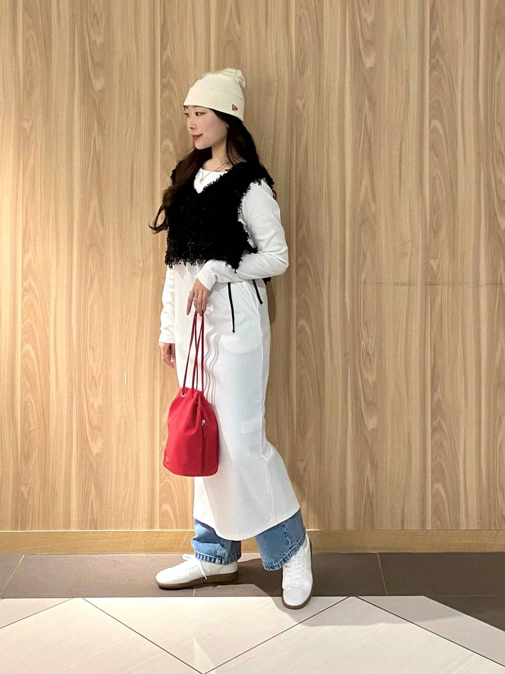 レッド系のハンドバッグ、ブルー系のデニムパンツ、ホワイト系のスニーカーを着用したレディースの冬コーディネートの2枚目の写真