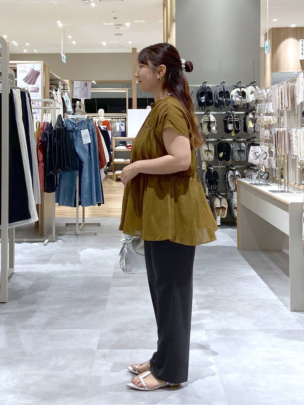 シルバー系のショルダーバッグ、ブラック系のスラックス、シルバー系のサンダルを着用したレディースの夏コーディネートの2枚目の写真