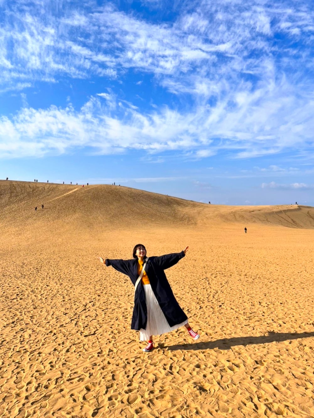 レッド系のスニーカー、ブルー系のトレンチコート、ホワイト系のショルダーバッグを着用したレディースの夏コーディネートの3枚目の写真