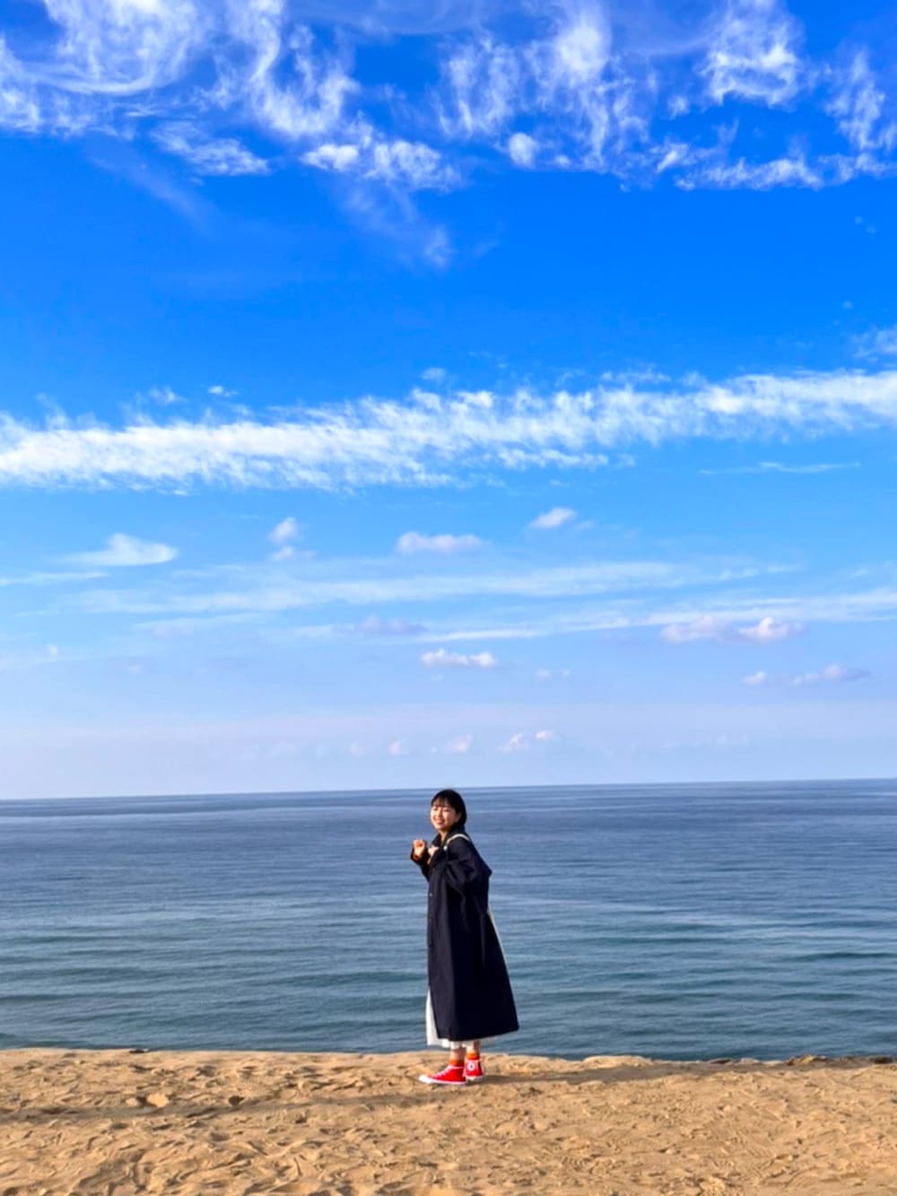 レッド系のスニーカー、ブルー系のトレンチコート、ホワイト系のショルダーバッグを着用したレディースの夏コーディネートの2枚目の写真