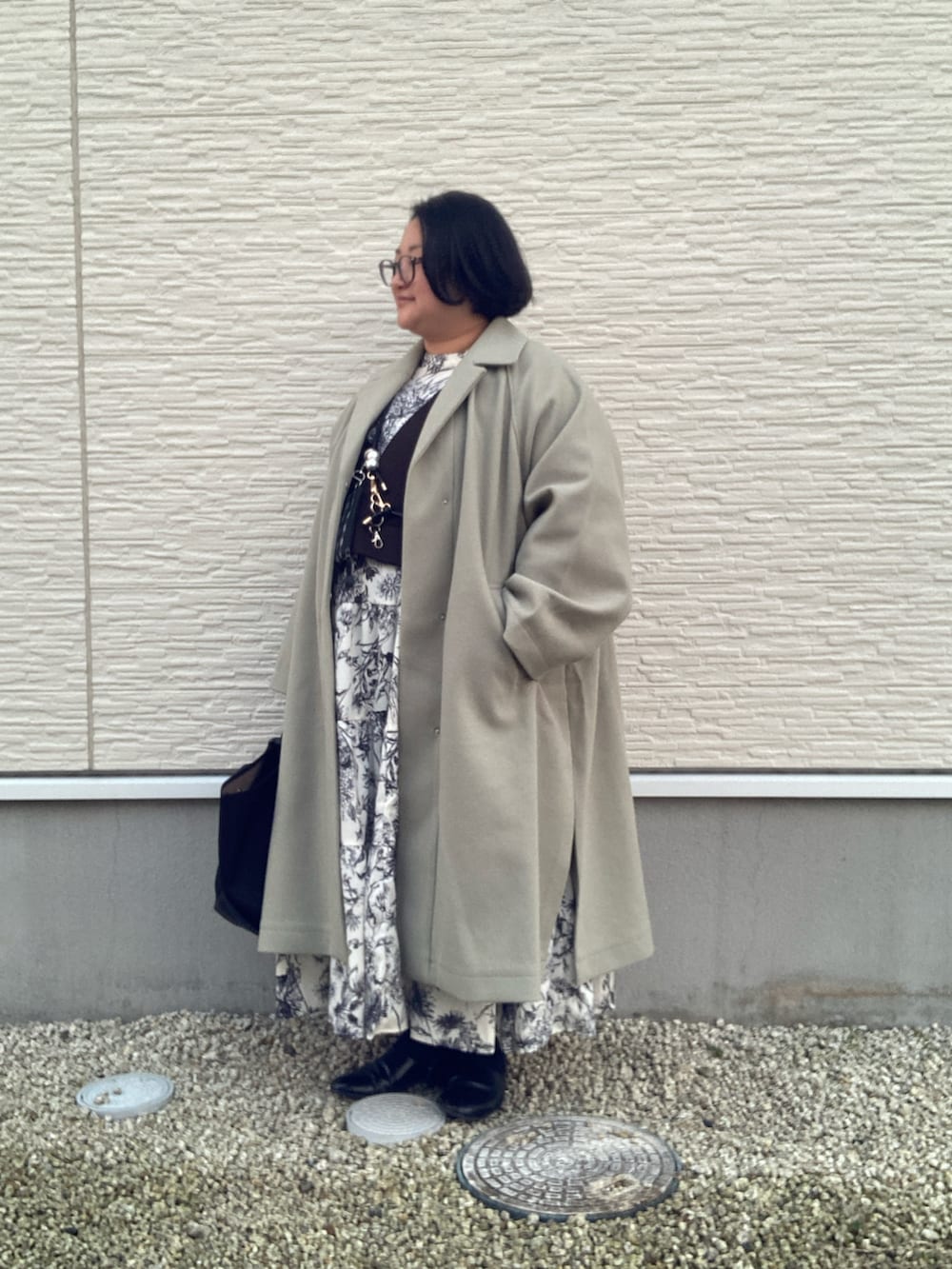 グリーン系のステンカラーコート、ホワイト系のシャツワンピース、ブラック系のベストを着用したレディースの冬コーディネートの2枚目の写真