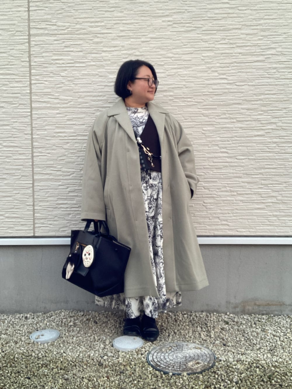 グリーン系のステンカラーコート、ホワイト系のシャツワンピース、ブラック系のベストを着用したレディースの冬コーディネートの5枚目の写真