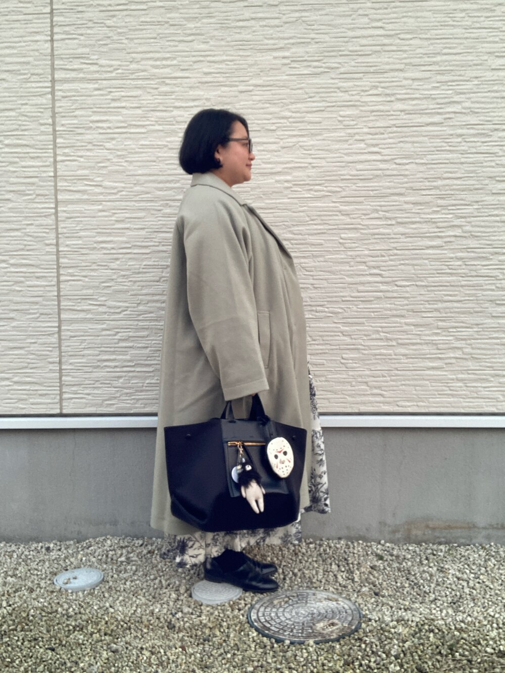 グリーン系のステンカラーコート、ホワイト系のシャツワンピース、ブラック系のベストを着用したレディースの冬コーディネートの3枚目の写真