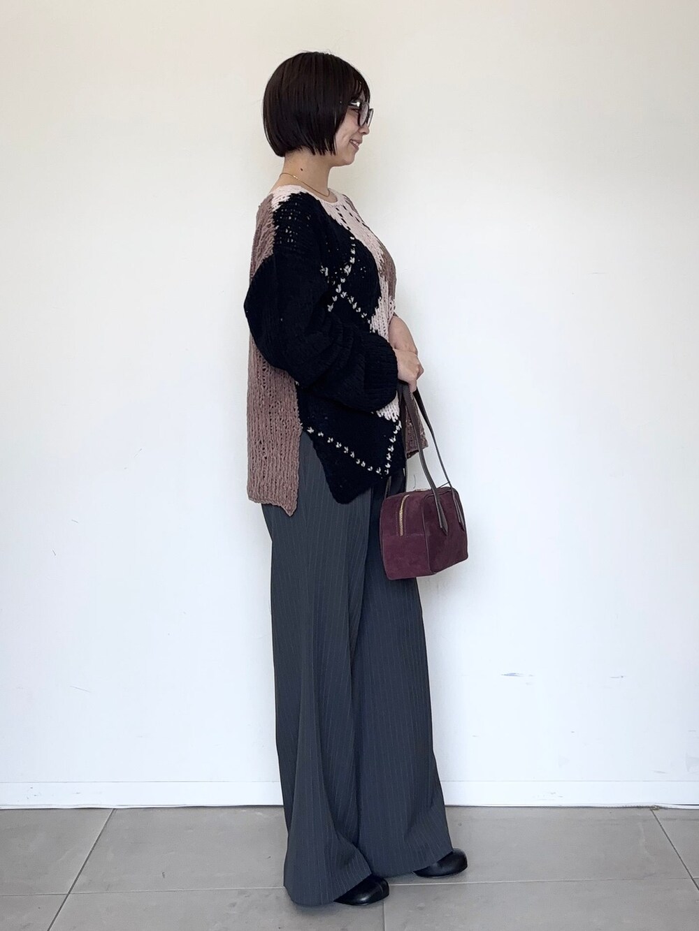 グレー系のスラックス、ブラウン系のニット/セーター、レッド系のボストンバッグを着用したレディースの秋コーディネートの4枚目の写真