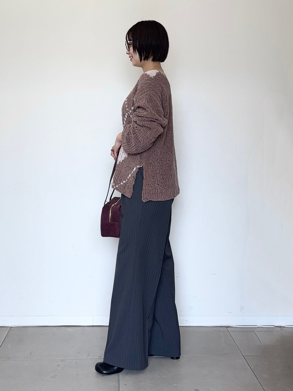 グレー系のスラックス、ブラウン系のニット/セーター、レッド系のボストンバッグを着用したレディースの秋コーディネートの2枚目の写真