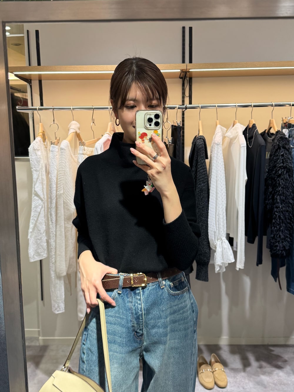 ブラック系のニット/セーター、ブルー系のデニムパンツ、ベージュ系のハンドバッグを着用したレディースの冬コーディネートの2枚目の写真