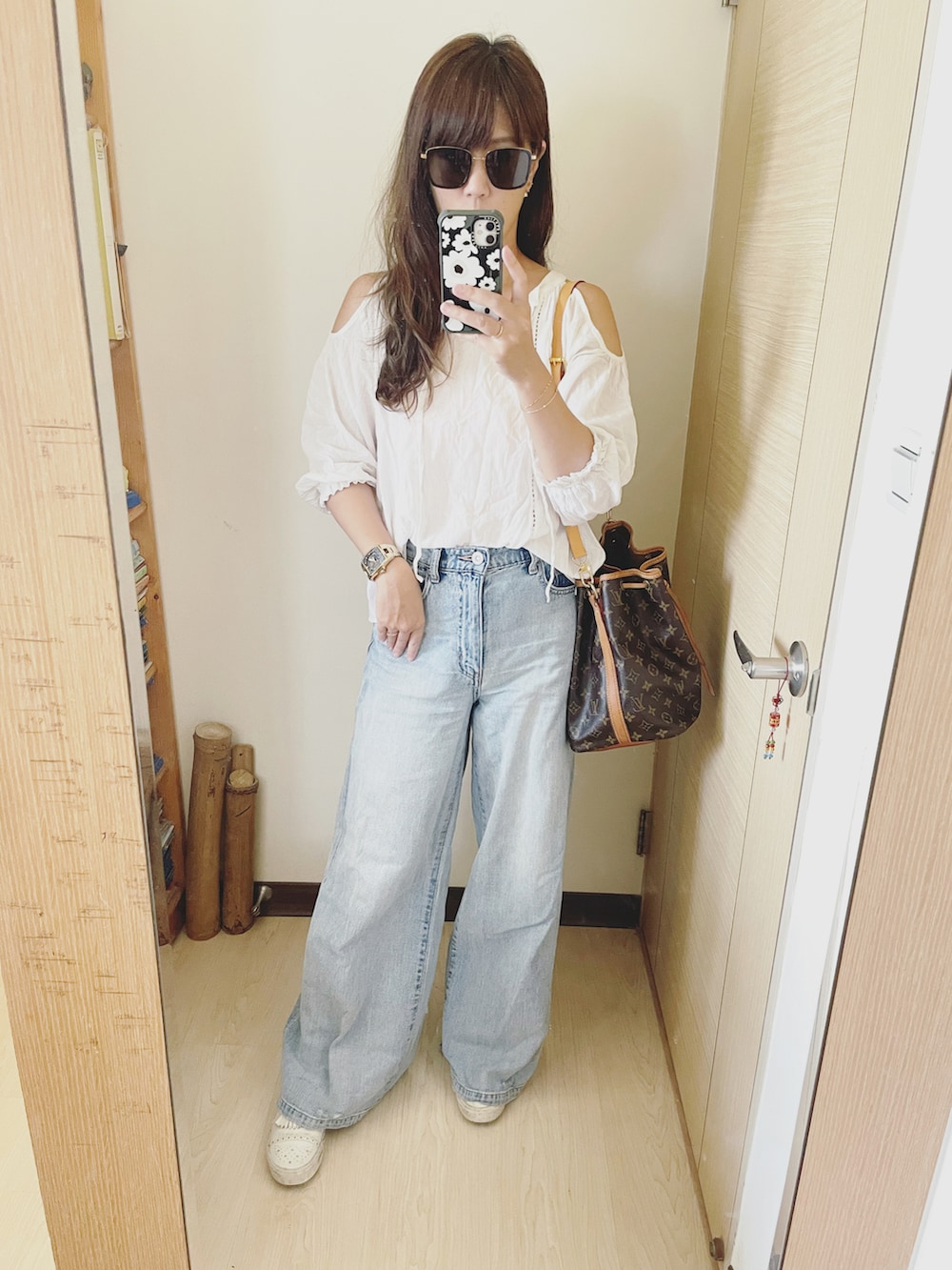 ブルー系のデニムパンツ、ブラウン系のバッグ、ホワイト系のシャツ/ブラウスを着用したレディースの夏コーディネートの2枚目の写真