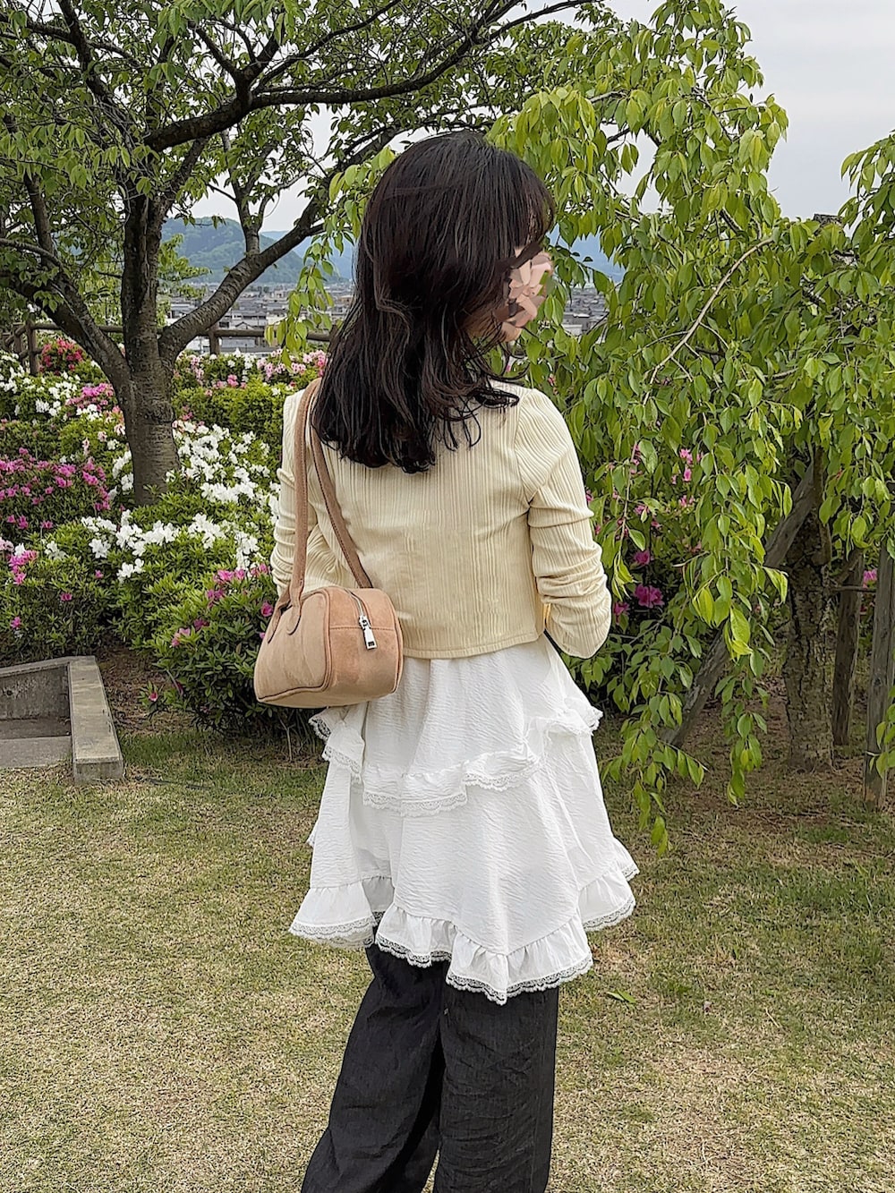 ベージュ系のボストンバッグ、ホワイト系のワンピース/ドレス、イエロー系のカーディガン/ボレロを着用したレディースの春コーディネートの2枚目の写真