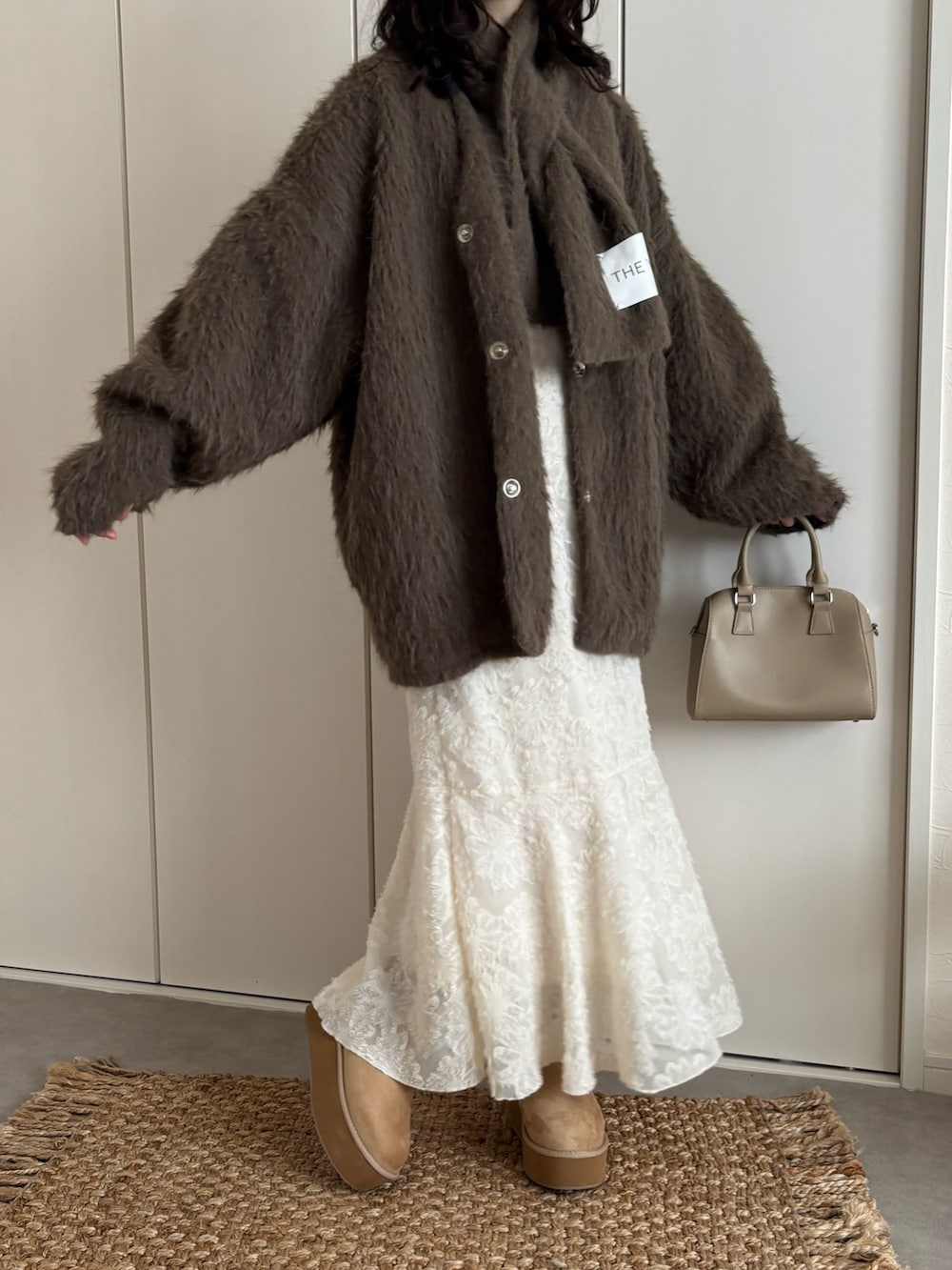ブラウン系のノーカラーコート、ホワイト系のワンピース、ベージュ系のブーツを着用したレディースの冬コーディネートの2枚目の写真
