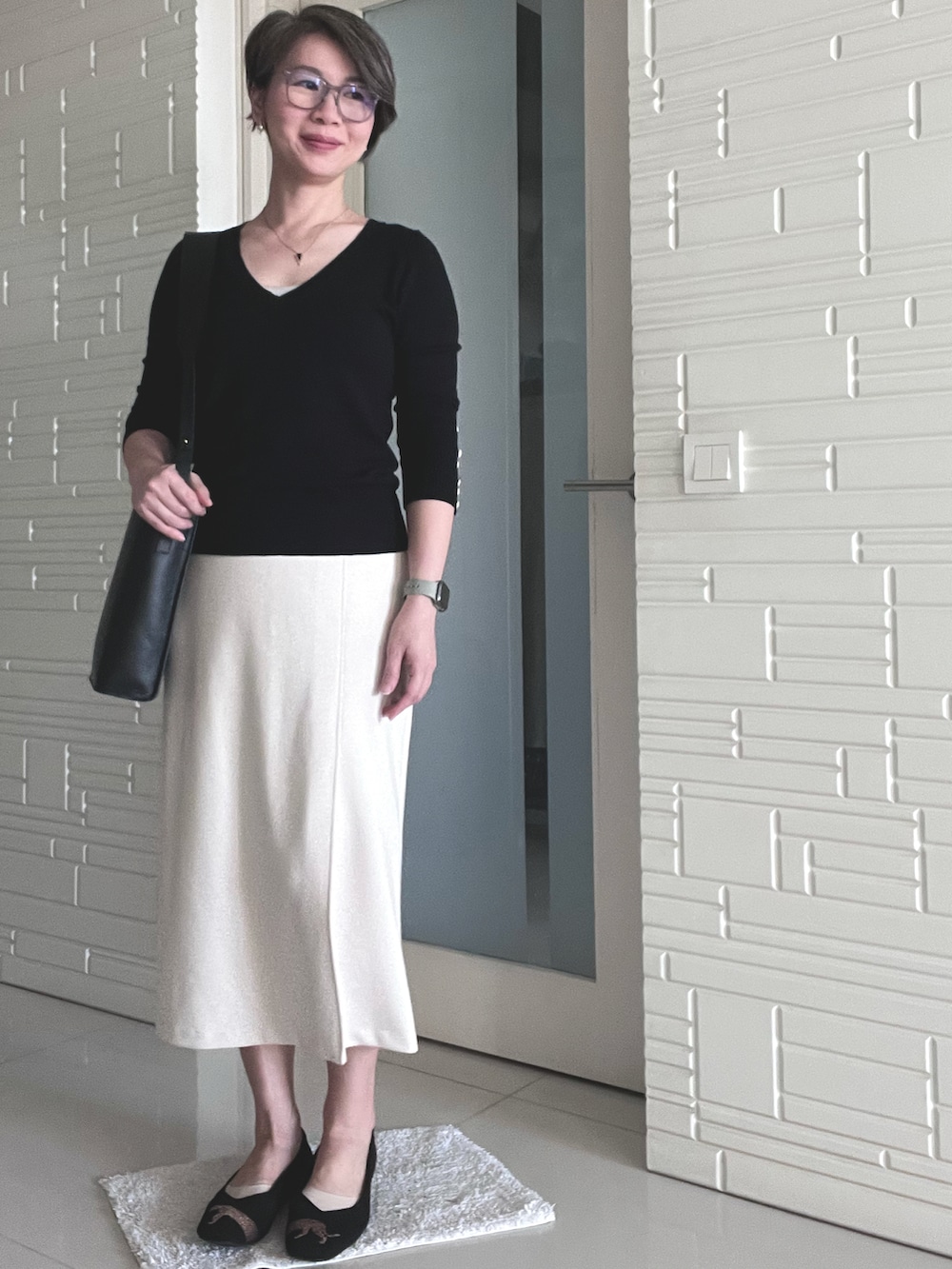 ベージュ系のスカート、ブラック系のニット/セーター、ブラック系のショルダーバッグを着用したレディースの春コーディネートの2枚目の写真