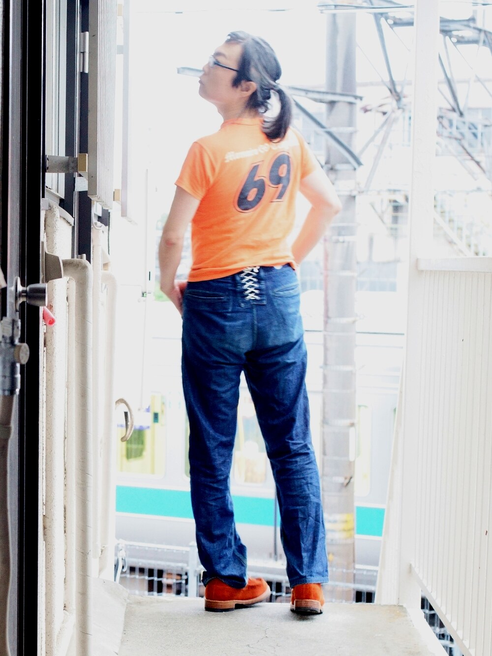 オレンジ系のTシャツ/カットソー、ブルー系のデニムパンツ、オレンジ系のブーツを着用したメンズの夏コーディネートの2枚目の写真