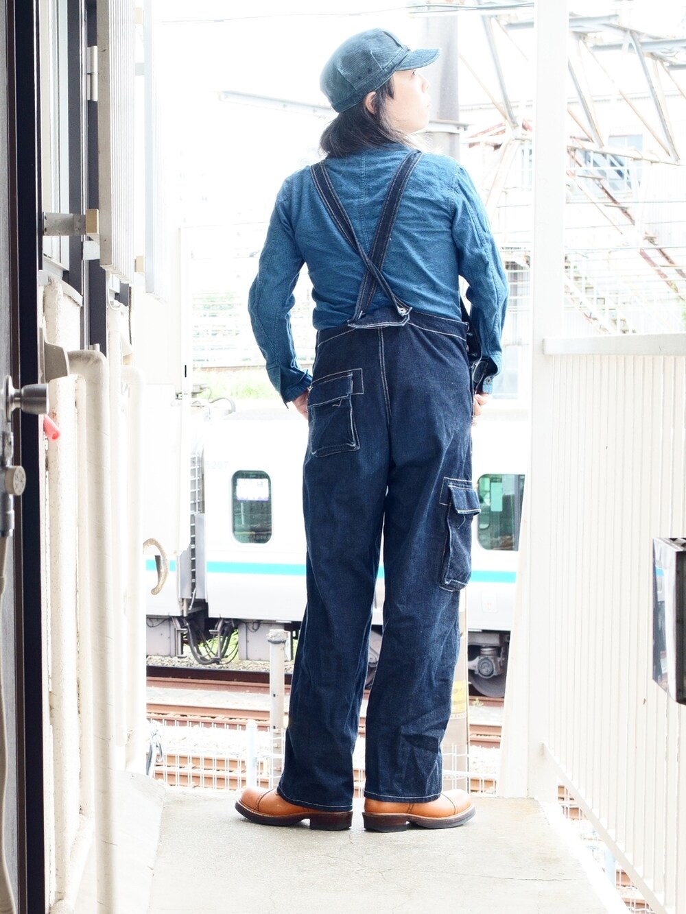 ブルー系のオールインワン・サロペット、オレンジ系のブーツ、ブルー系のキャップを着用したメンズの夏コーディネートの2枚目の写真