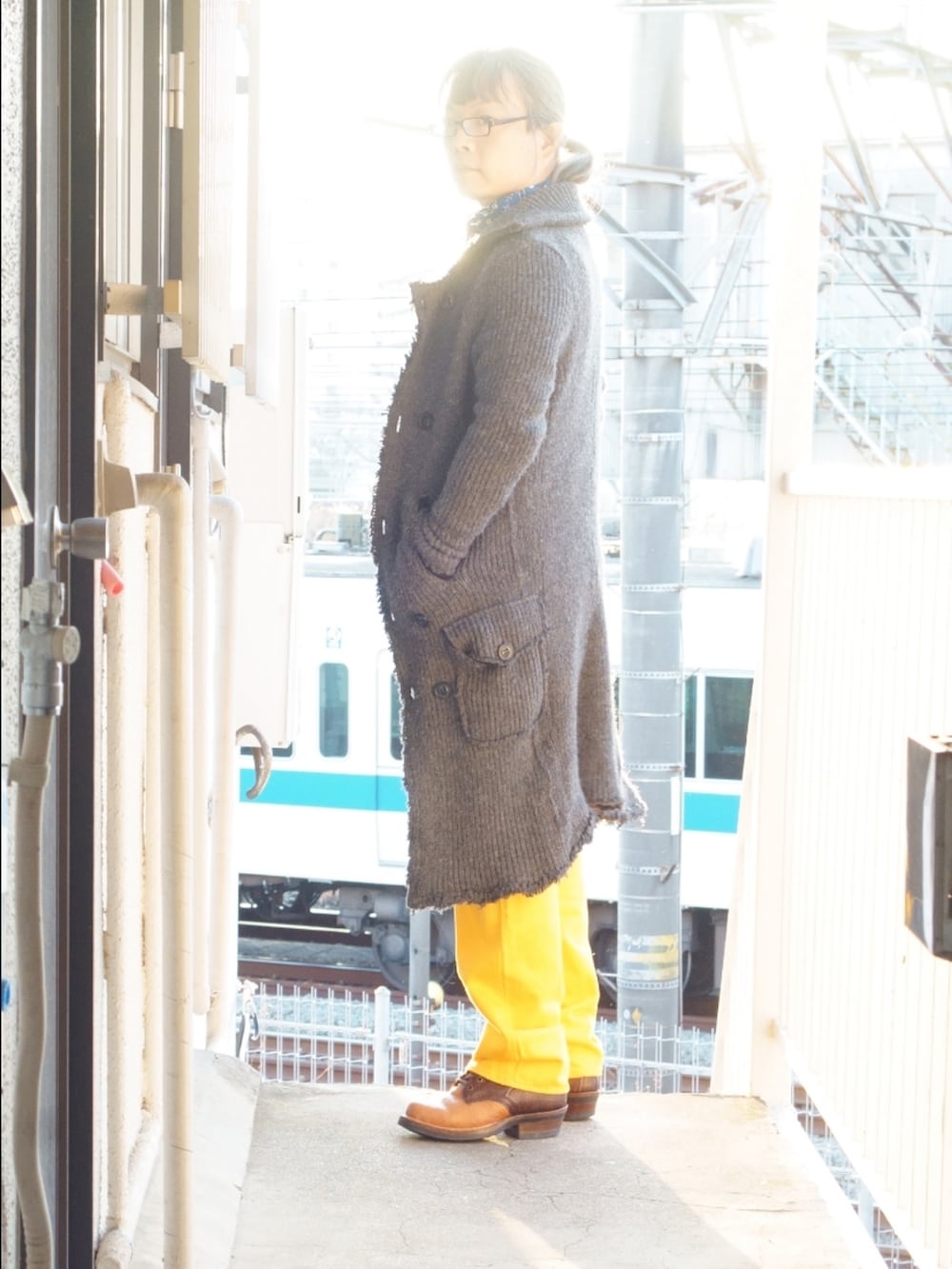 イエロー系のデニムパンツ、ブラウン系のブーツ、グレー系のピーコートを着用したメンズの夏コーディネートの2枚目の写真