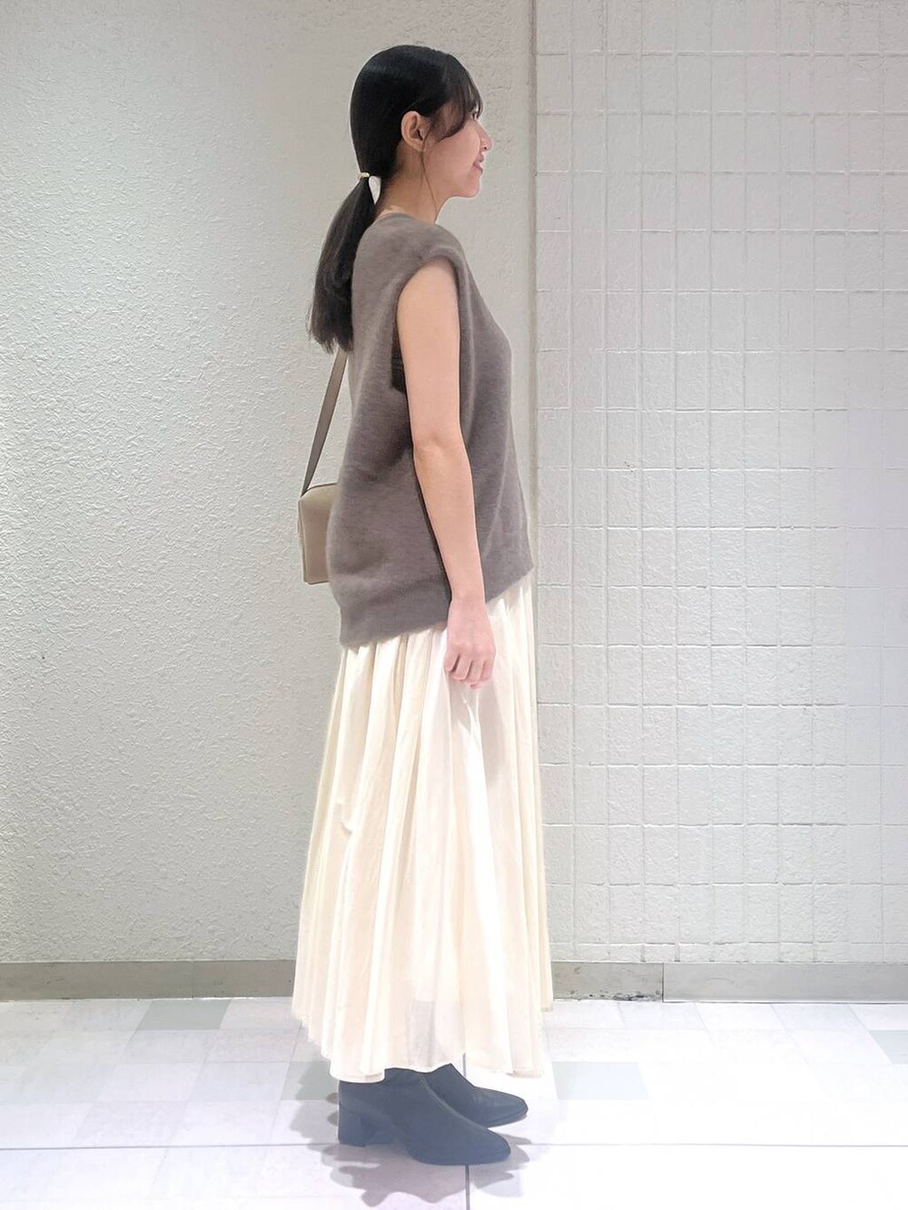 ブラック系のブーツ、ブラウン系のベスト、ホワイト系のスカートを着用したレディースの秋コーディネートの2枚目の写真