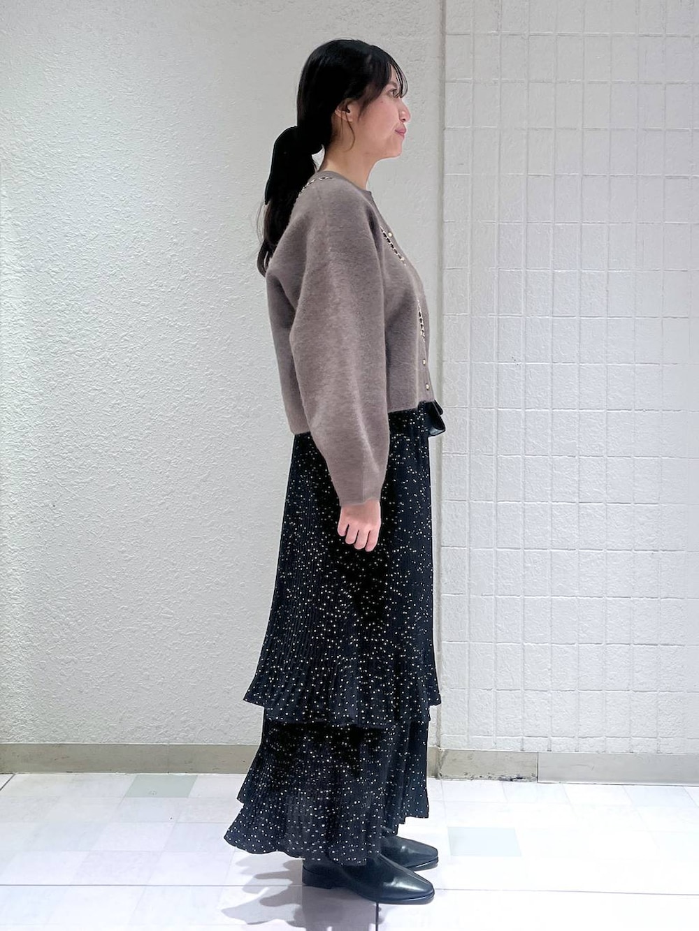 グレー系のスカート、ブラック系のブーツ、ゴールド系のネックレスを着用したレディースの秋コーディネートの2枚目の写真