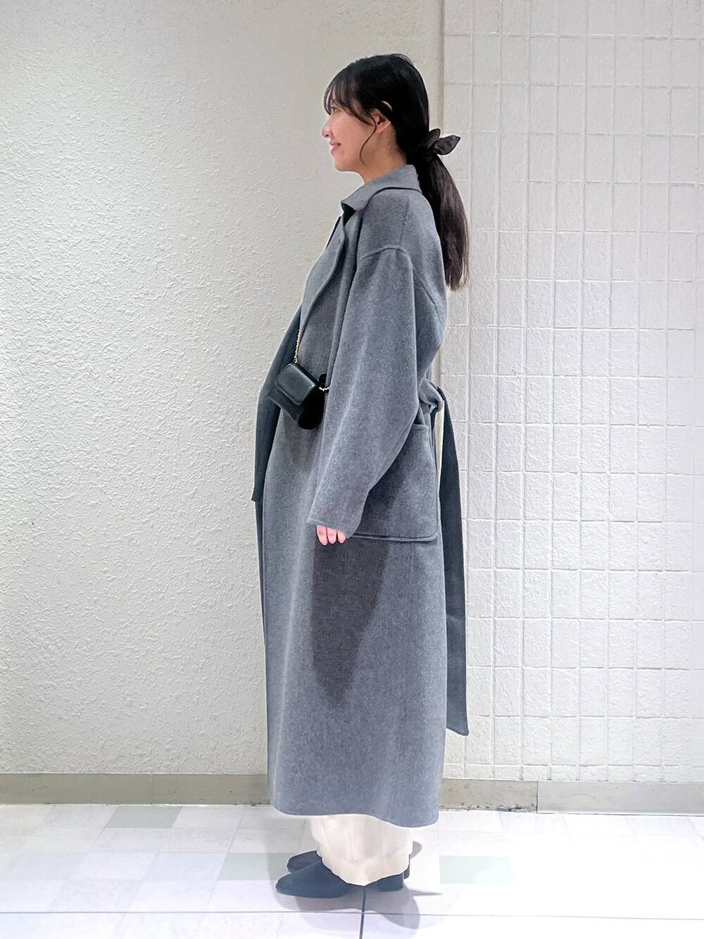 グレー系のステンカラーコート、ホワイト系のスラックス、ブラック系のブーツを着用したレディースの秋コーディネートの3枚目の写真