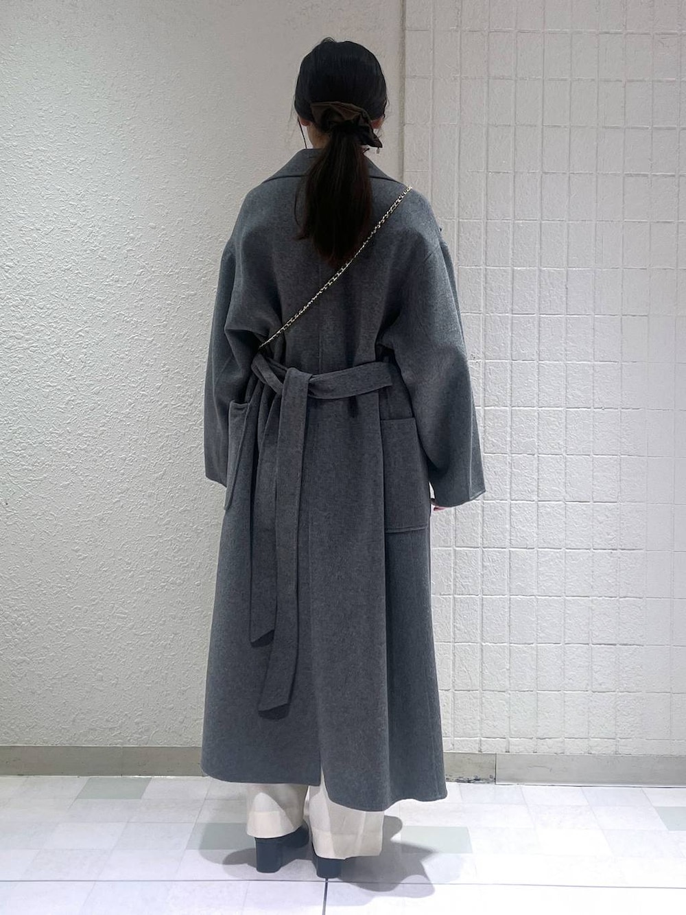 グレー系のステンカラーコート、ホワイト系のスラックス、ブラック系のブーツを着用したレディースの秋コーディネートの4枚目の写真