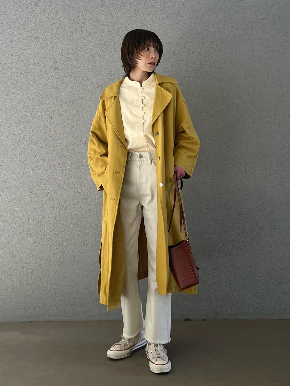 イエロー系のチェスターコート、ブラウン系のショルダーバッグ、ホワイト系のデニムパンツを着用したレディースの春コーディネートの2枚目の写真