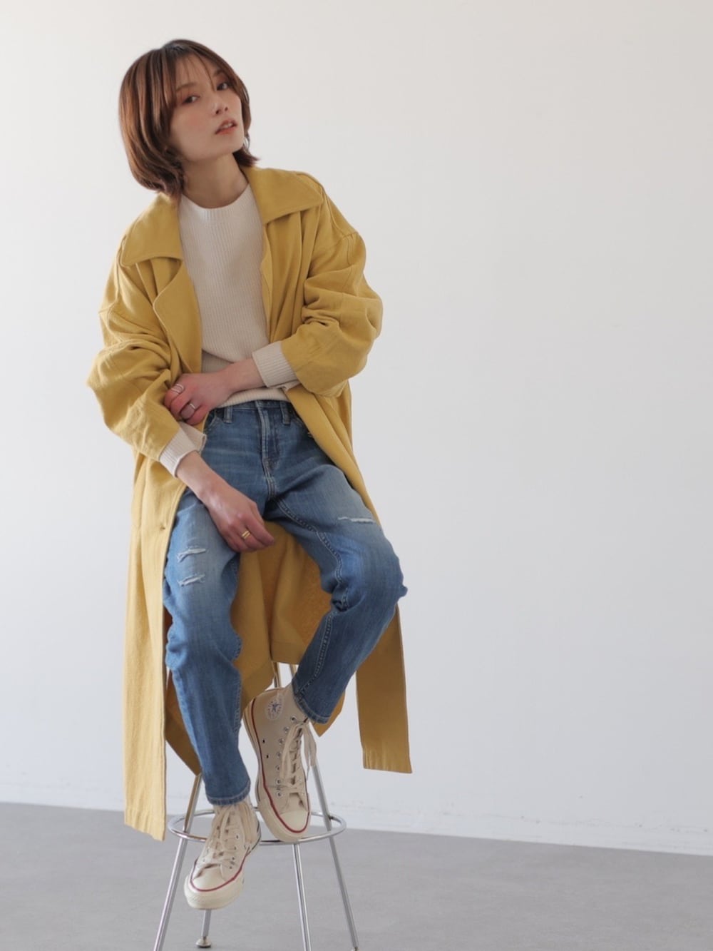ブルー系のデニムパンツ、イエロー系のチェスターコート、ホワイト系のTシャツ/カットソーを着用したレディースの冬コーディネートの2枚目の写真