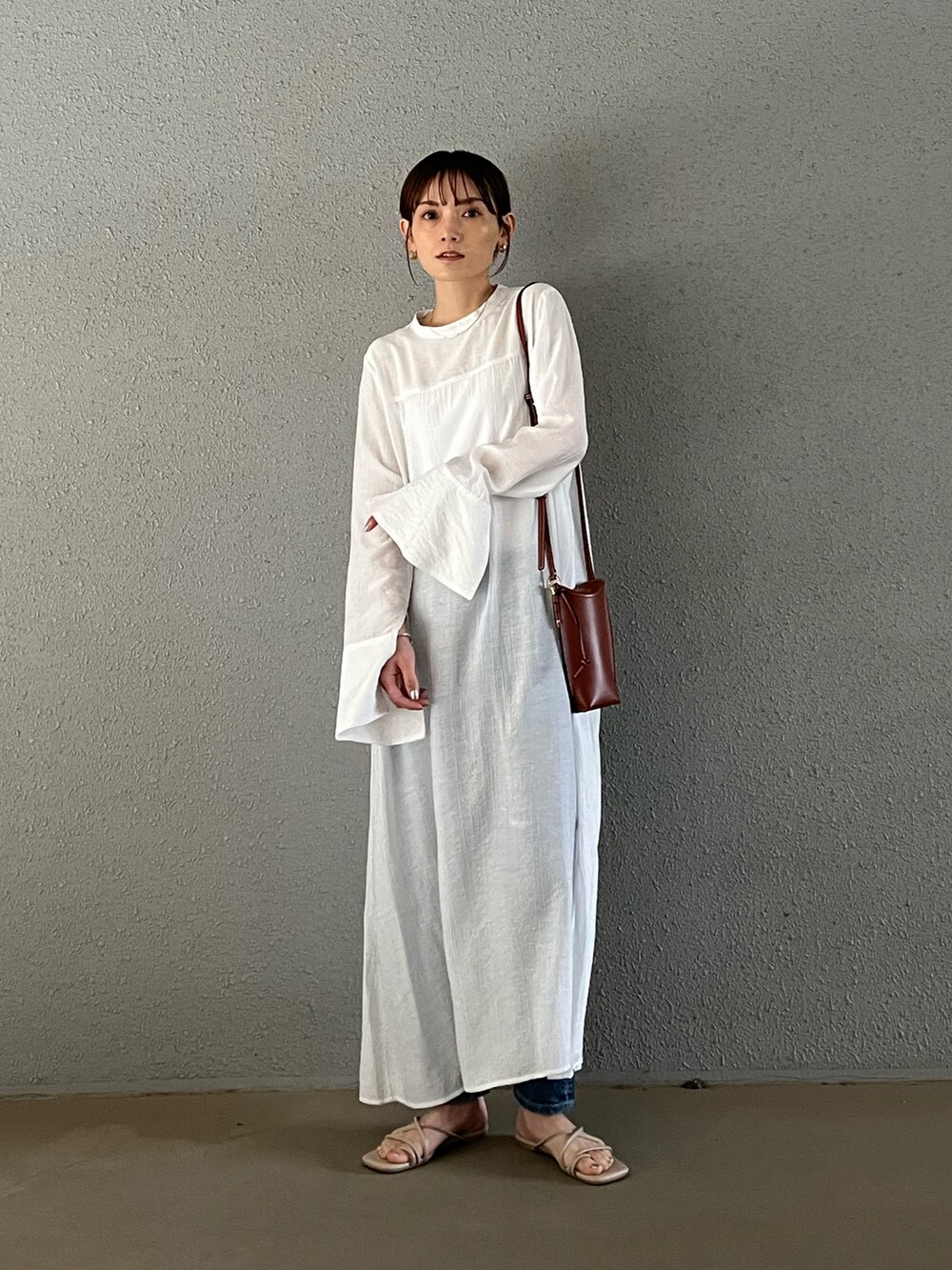 ホワイト系のワンピース、ベージュ系のサンダル、ブルー系のデニムパンツを着用したレディースの春コーディネートの2枚目の写真