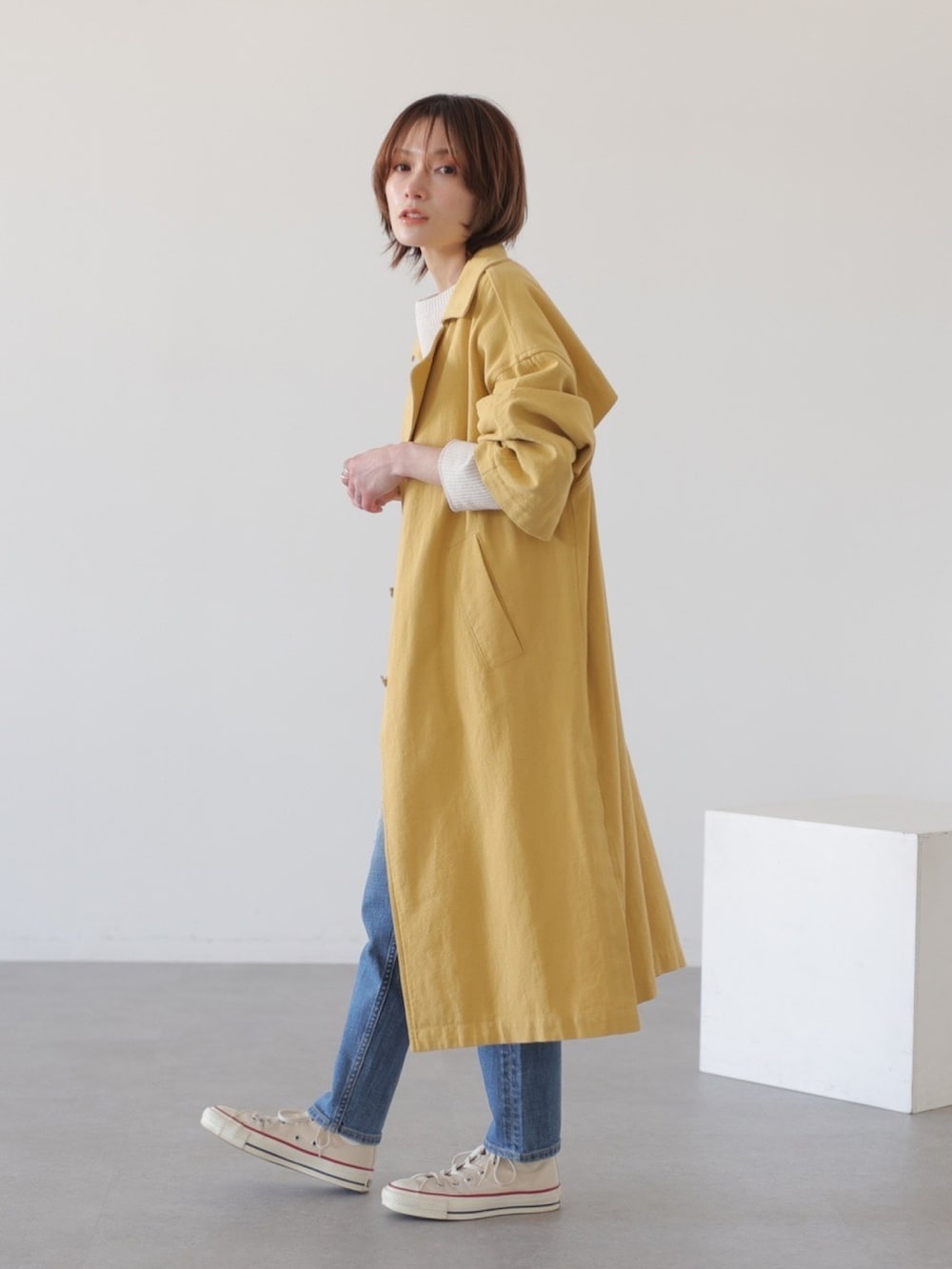 ブルー系のデニムパンツ、イエロー系のチェスターコート、ホワイト系のTシャツ/カットソーを着用したレディースの冬コーディネートの3枚目の写真