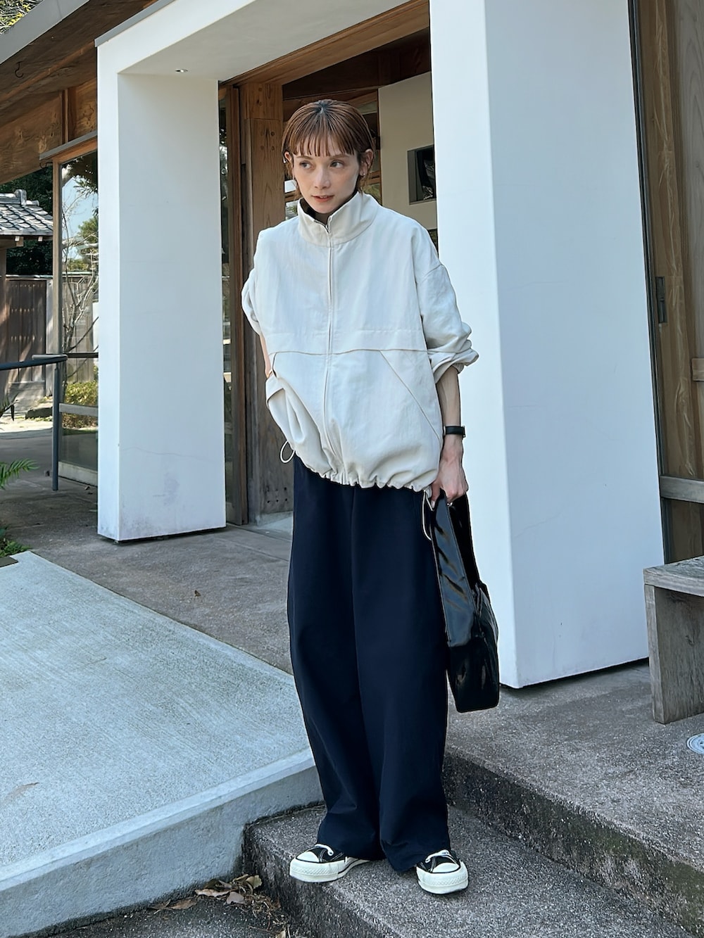 ホワイト系のブルゾン、ブルー系のパンツ、ブラック系のバッグを着用したレディースの春コーディネートの2枚目の写真