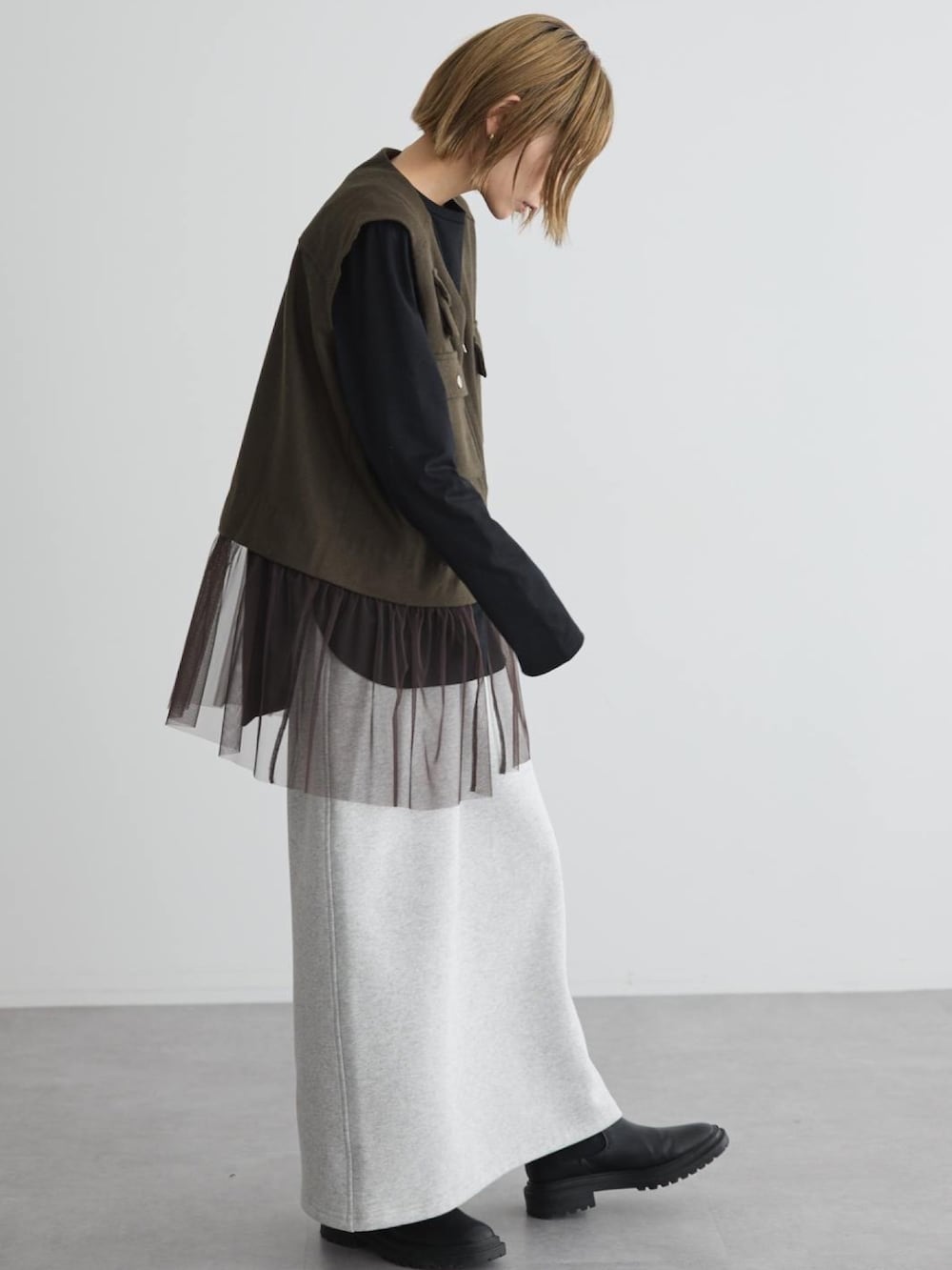 グリーン系のベスト、ブラック系のブーツを着用したレディースの秋コーディネートの2枚目の写真