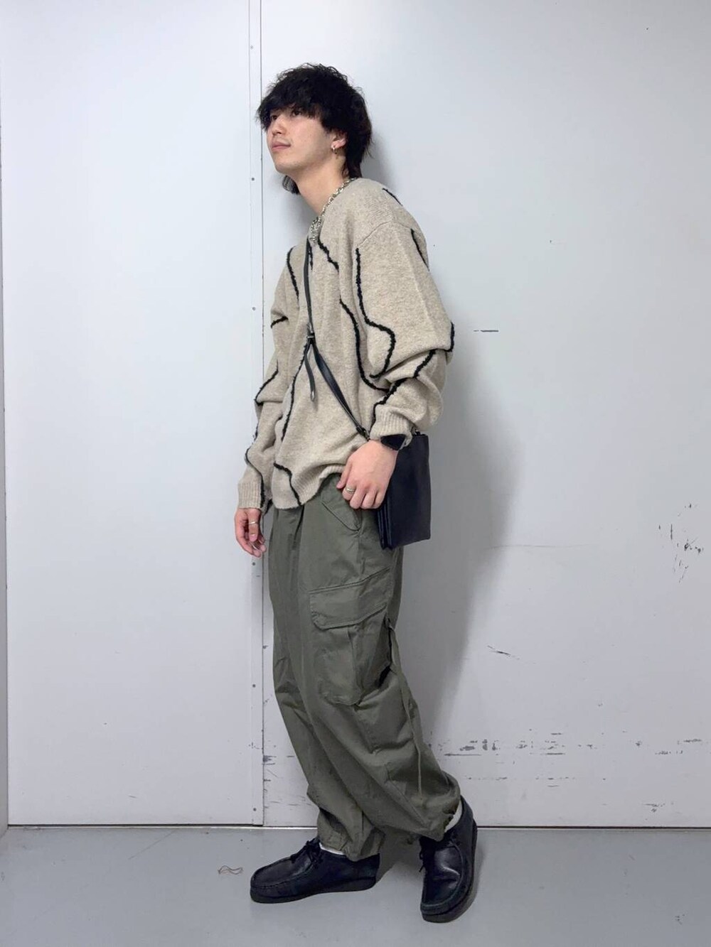 グリーン系のカーゴパンツ、ベージュ系のニット/セーター、ブラック系のショルダーバッグを着用したメンズの秋コーディネートの2枚目の写真