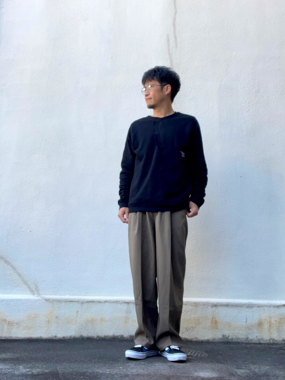 ブラウン系のスラックス、ブラック系のスウェット、ブルー系のスニーカーを着用したメンズの春コーディネートの2枚目の写真