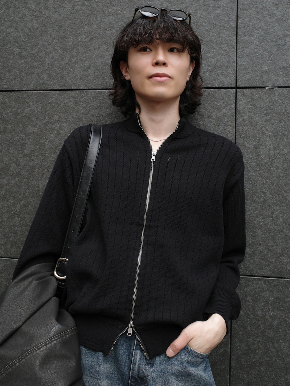 グレー系のブルゾン、ブラック系のショルダーバッグ、ブルー系のデニムパンツを着用したメンズの秋コーディネートの3枚目の写真