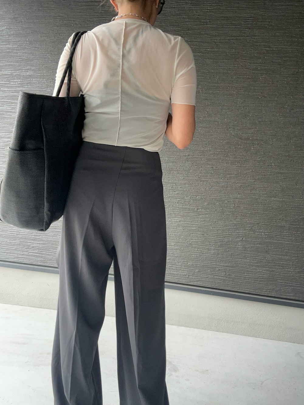 ブラック系のトートバッグ、グレー系のスラックス、ホワイト系のトップスを着用したレディースの夏コーディネートの3枚目の写真