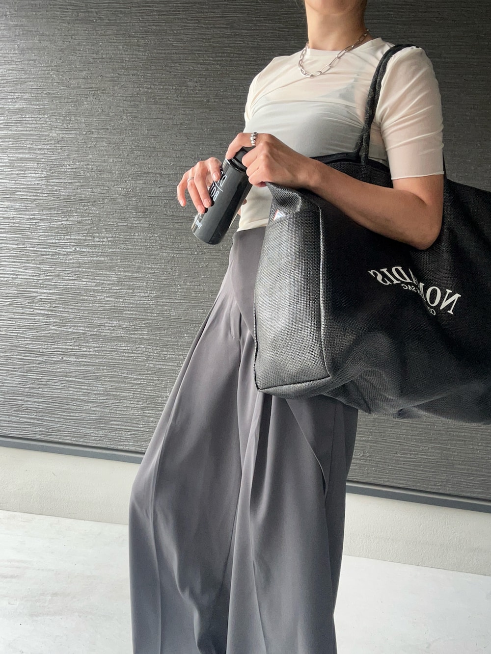 ブラック系のトートバッグ、グレー系のスラックス、ホワイト系のトップスを着用したレディースの夏コーディネートの2枚目の写真