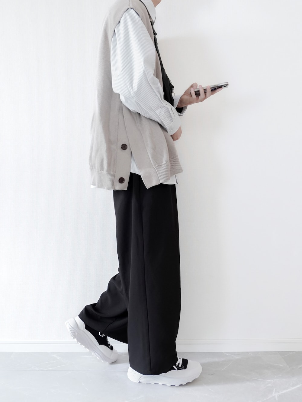 ベージュ系のベスト、ブラック系のスラックス、ブラック系のスニーカーを着用したメンズの春コーディネートの2枚目の写真