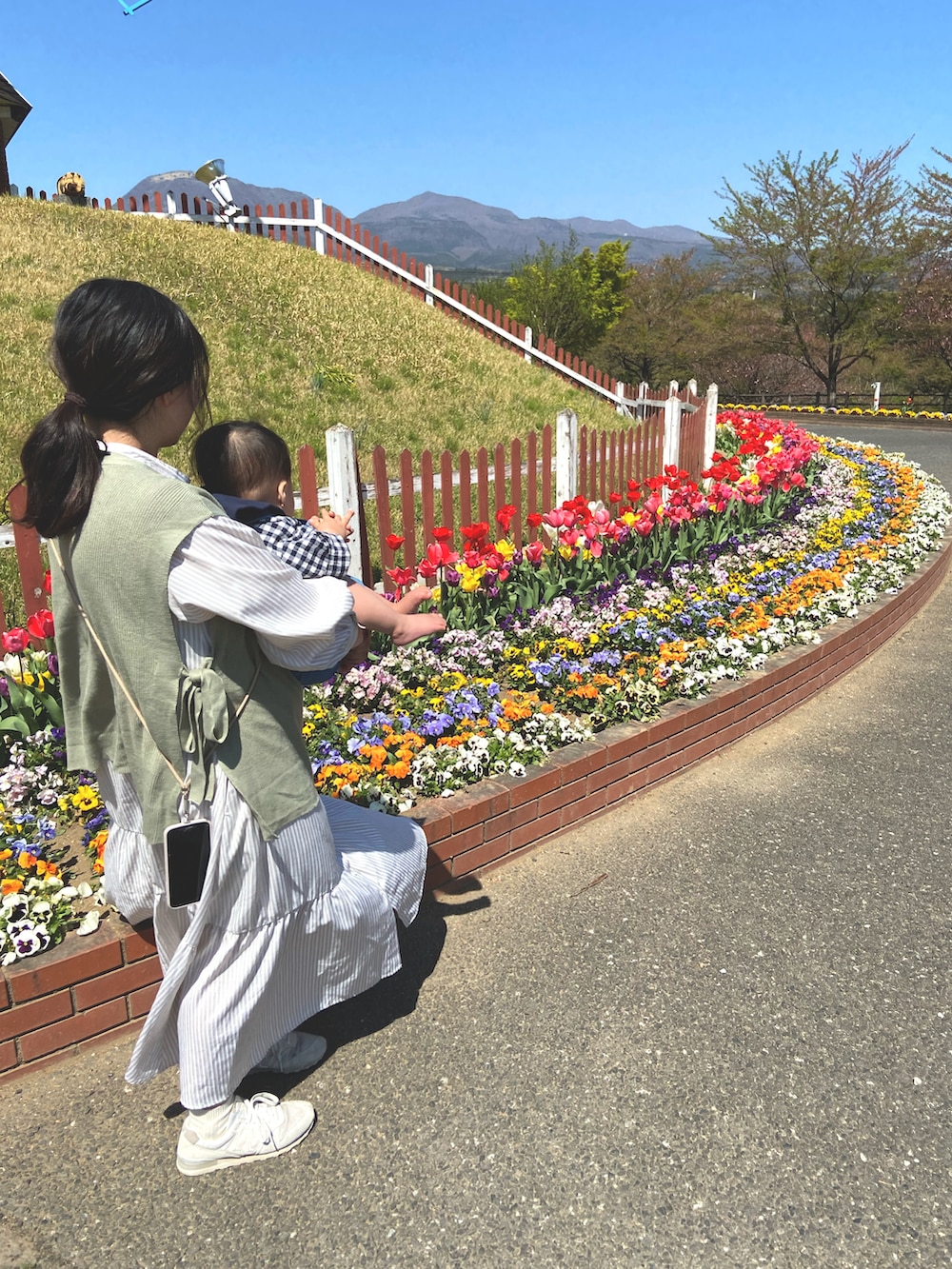 ベージュ系のシャツワンピース、グリーン系のベスト、ホワイト系のスニーカーを着用したレディースの春コーディネートの2枚目の写真