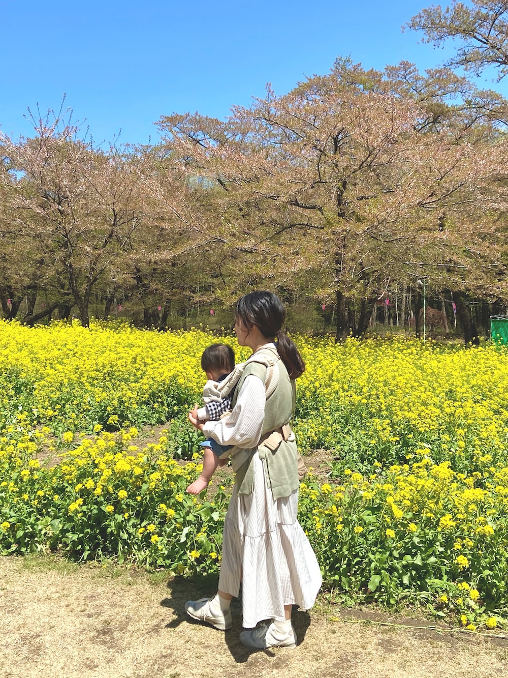 ベージュ系のシャツワンピース、グリーン系のベスト、ホワイト系のスニーカーを着用したレディースの春コーディネートの3枚目の写真