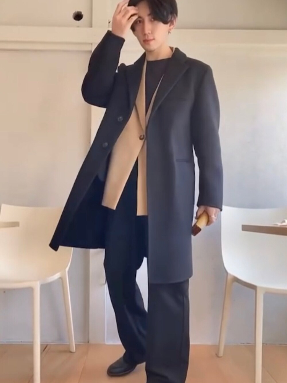 ブラック系のノーカラーコート、ベージュ系のベスト、ブラック系のスラックスを着用したメンズの冬コーディネートの2枚目の写真