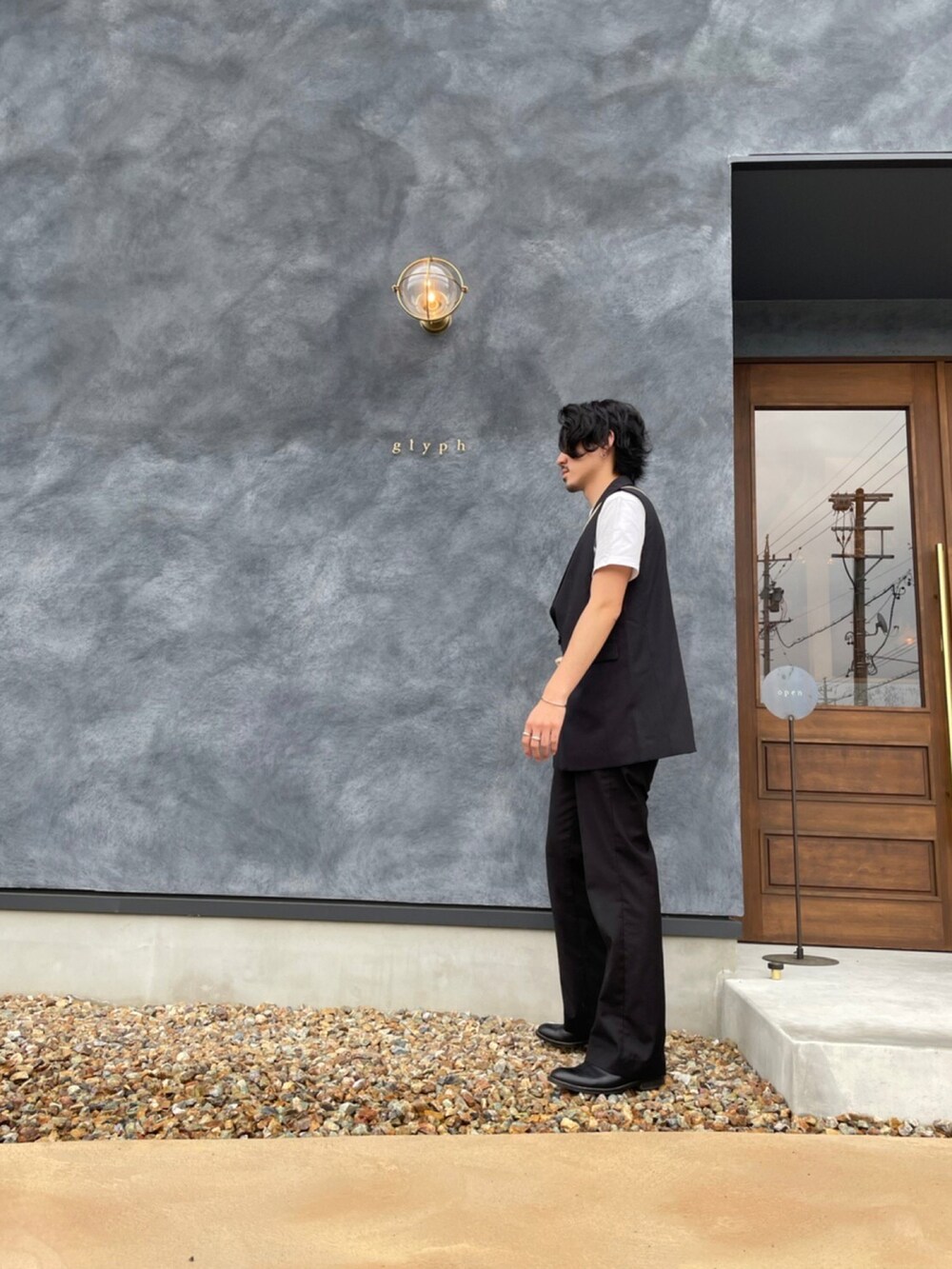 ブラック系のベスト、ブラック系のスラックス、ベージュ系のショルダーバッグを着用したメンズの春コーディネートの2枚目の写真