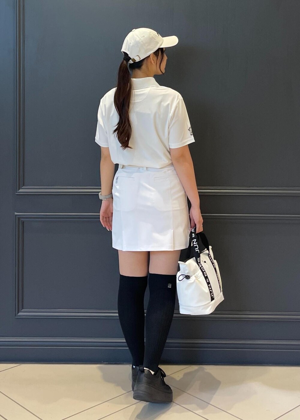 ホワイト系のハンドバッグ、ホワイト系のスカート、ホワイト系のポロシャツを着用したレディースの夏コーディネートの2枚目の写真