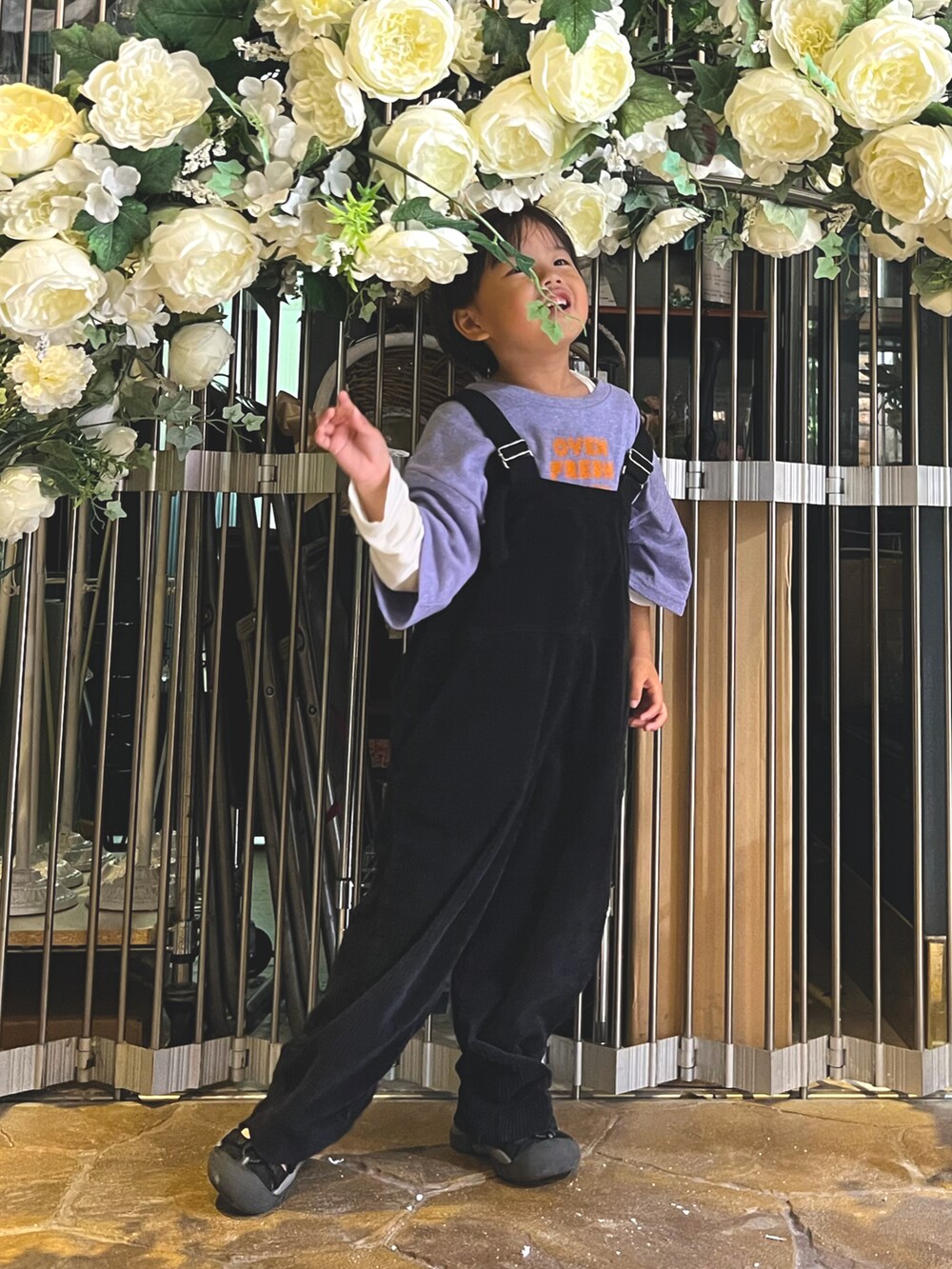 ブラック系のサロペット/オーバーオール、パープル系のTシャツ/カットソー、ブラック系のサンダルを着用したキッズの冬コーディネートの2枚目の写真