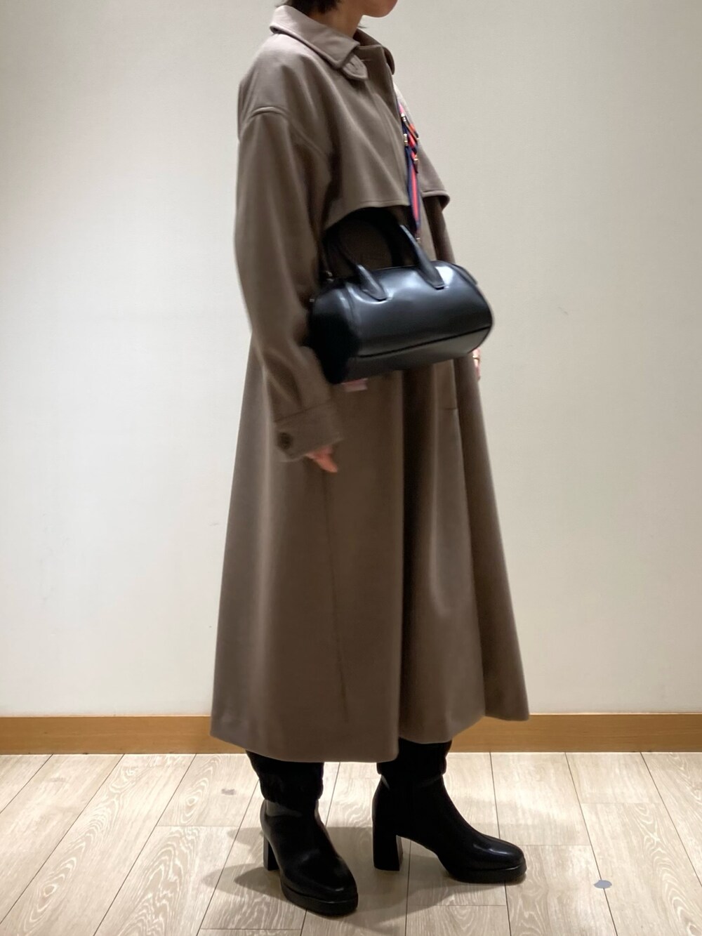 ブラウン系のステンカラーコート、ブラック系のボストンバッグ、ブラック系のブーツを着用したレディースの冬コーディネートの4枚目の写真