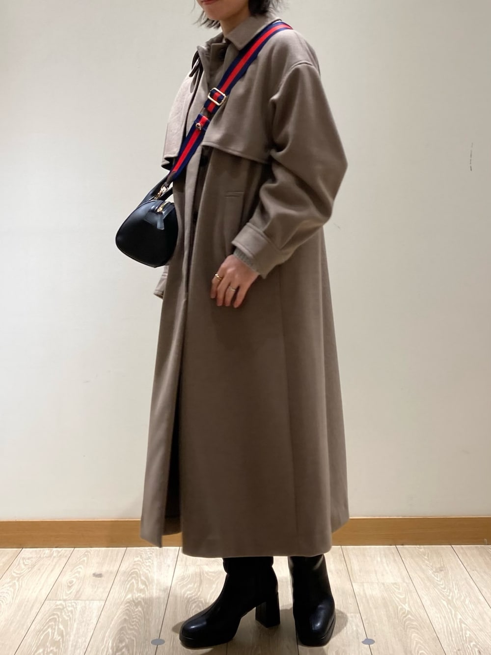 ブラウン系のステンカラーコート、ブラック系のボストンバッグ、ブラック系のブーツを着用したレディースの冬コーディネートの7枚目の写真